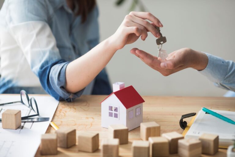 close-up-woman-s-hand-giving-house-key-man-wooden-table