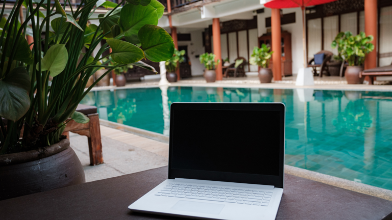 A laptop placed near a serene poolside in Bali, symbolizing the rise of digital nomad-friendly accommodations in Bali’s real estate trends.