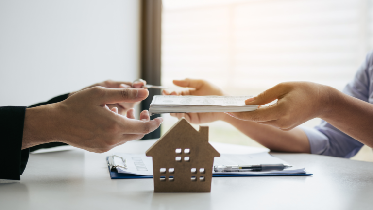 A close-up of hands exchanging cash during a property transaction, with a small model house in the foreground, highlighting concerns about fraudulent property brokers in real estate dealings.