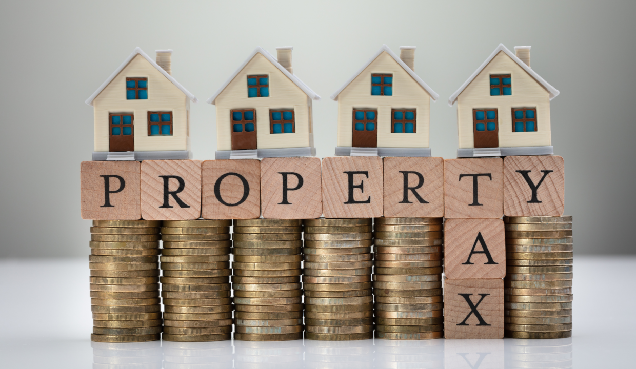 Mini houses on stacked coins spelling "PROPERTY TAX," illustrating how to invest dividends in property and reduce taxes.