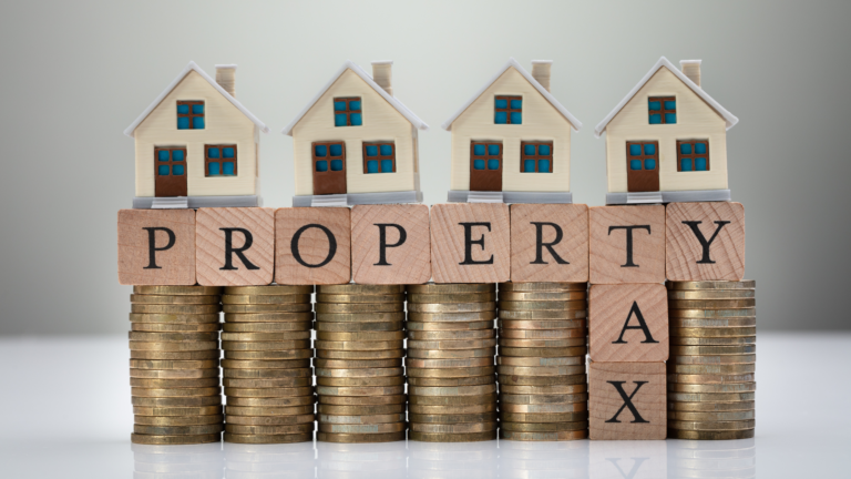 Mini houses on stacked coins spelling "PROPERTY TAX," illustrating how to invest dividends in property and reduce taxes.