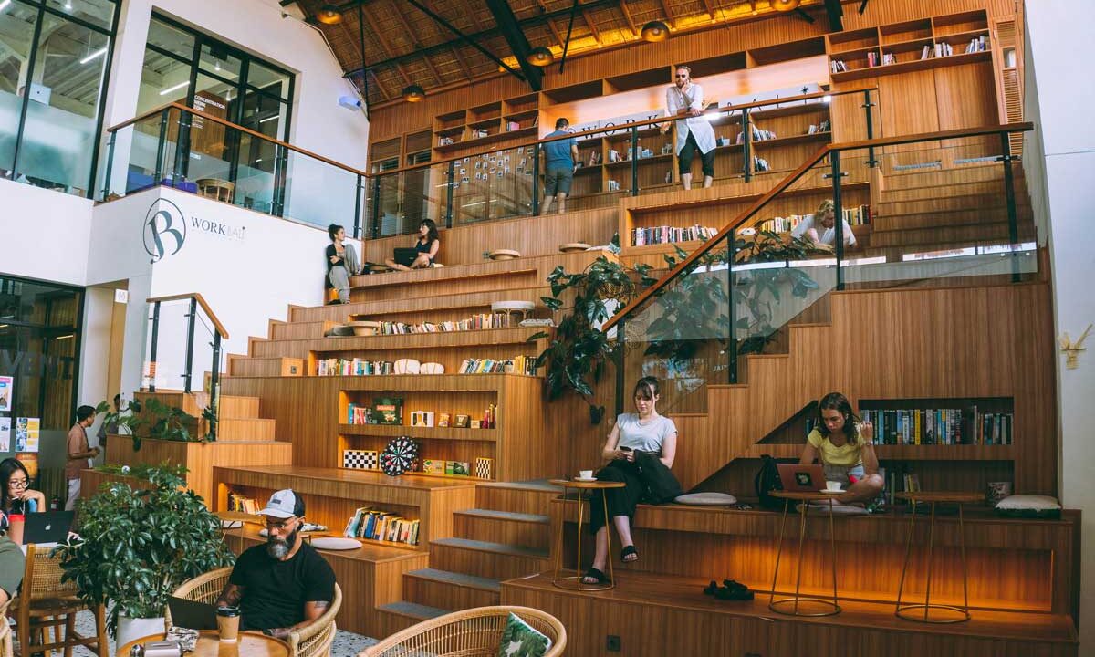 People working and reading in a tiered wooden seating area at BWork, a popular co-working space in Bali.