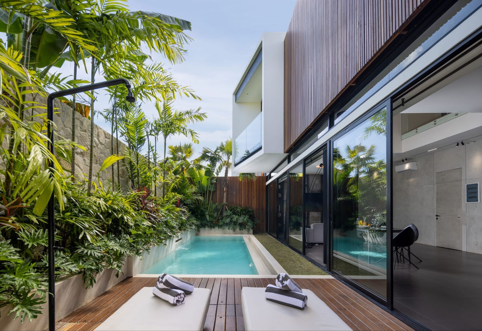 A charming outdoor scene at a Canggu Bali villa, with a private swimming pool, sun loungers on a wooden deck, and dense tropical foliage.