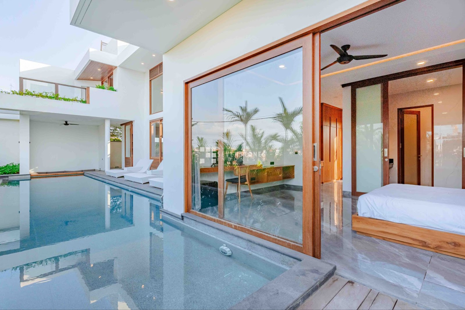 A bright and airy bedroom and office space of a Canggu Bali villa, with large glass doors opening to a private swimming pool.