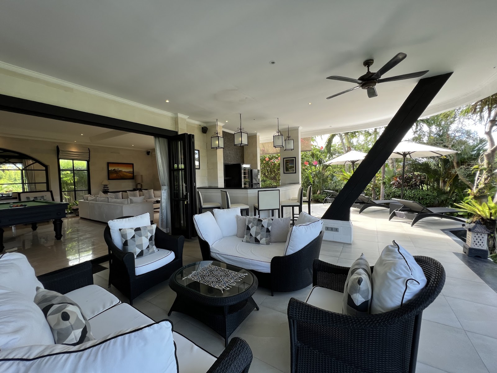 A spacious outdoor living and entertaining area of a luxurious Canggu Bali villa, with comfortable seating, a bar, and a view of the tropical garden.