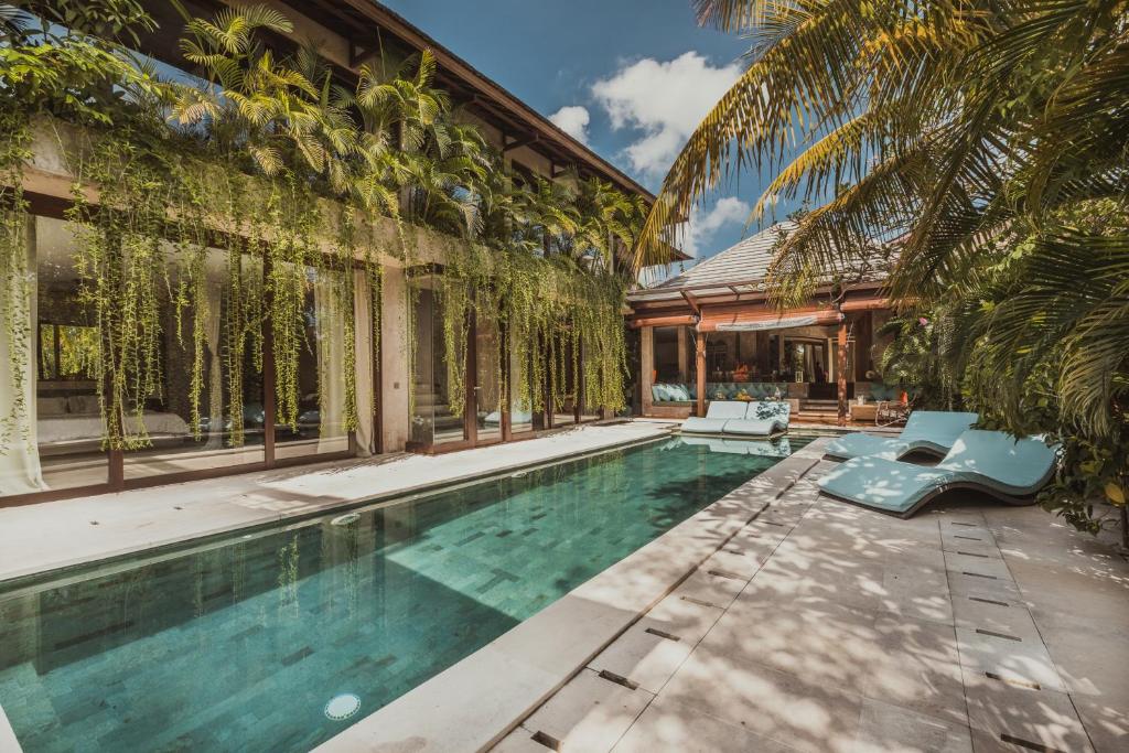 An expansive outdoor area of a luxury Canggu Bali villa, featuring a long swimming pool surrounded by lush tropical plants and lounge chairs.