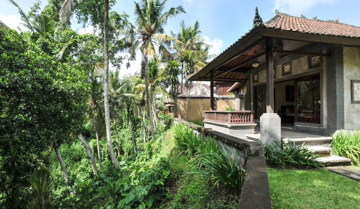 A Balinese style house in Ubud surrounded by lush tropical greenery, featuring traditional architecture with a thatched roof and open-air veranda.