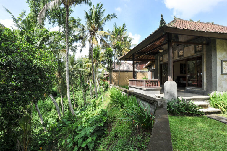 A Balinese style house in Ubud surrounded by lush tropical greenery, featuring traditional architecture with a thatched roof and open-air veranda.