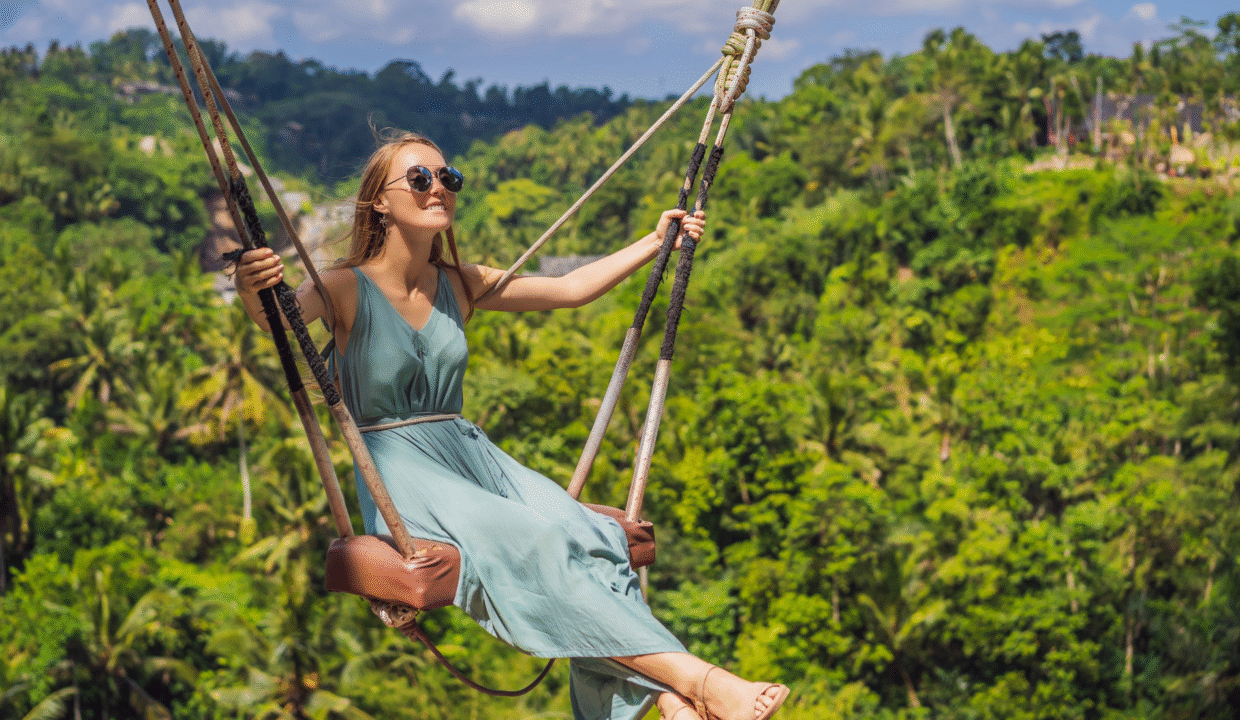 A woman enjoys a thrilling ride on a giant jungle swing in Bali, Indonesia, surrounded by lush green tropical forest - one of the top outdoor activities in Bali, Indonesia.