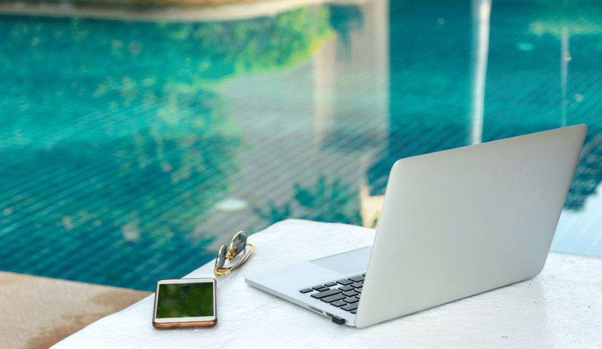 Laptop, smartphone, and sunglasses on a poolside table at a villa — ideal remote work setup for digital nomads in Bali.