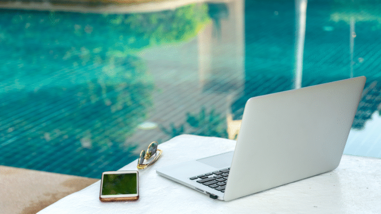Laptop, smartphone, and sunglasses on a poolside table at a villa — ideal remote work setup for digital nomads in Bali.