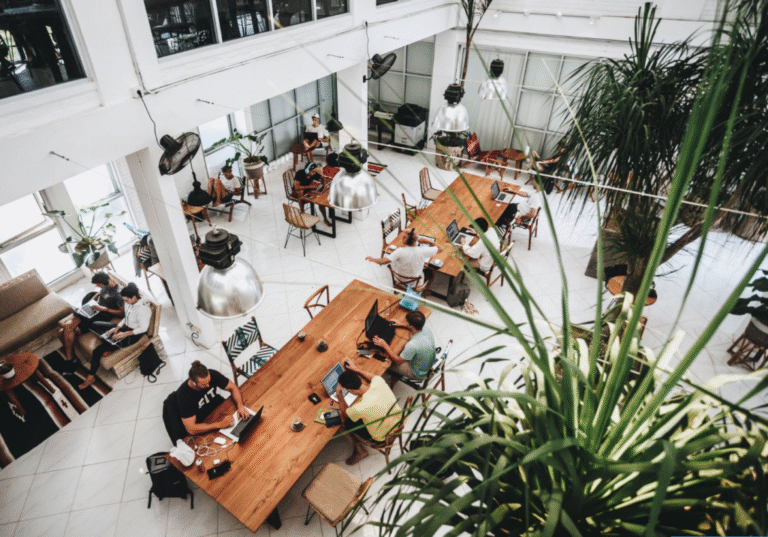 Remote workers at a vibrant coworking space in Bali, featuring long communal tables, natural light, and tropical indoor plants.