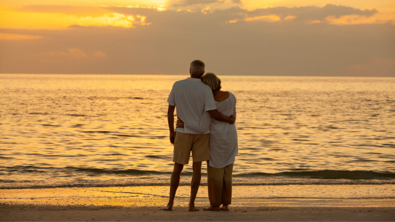 Elderly couple embracing on a Bali beach at sunset, symbolizing the peaceful lifestyle of retiring in Bali.
