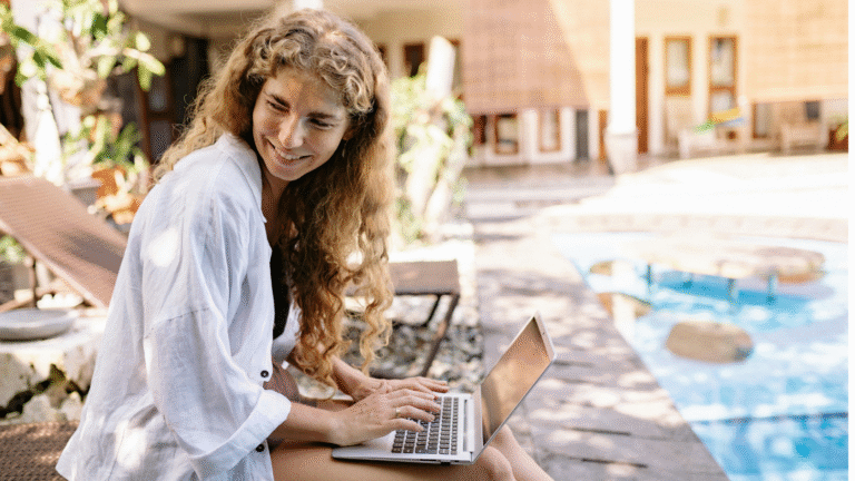 A woman working from her laptop beside a pool as a digital nomad in Bali.
