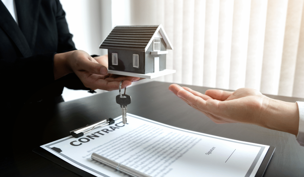 A person handing over house keys and a miniature home model above a signed document, illustrating a Villa Rental Contract in Indonesia.