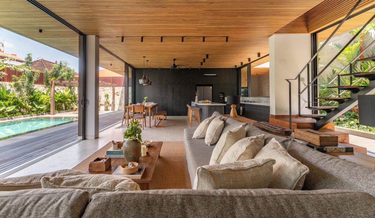 A spacious open-plan living area in a modern tropical home with poolside views, showcasing the comfort and style offered by family villas for rent in Bali.