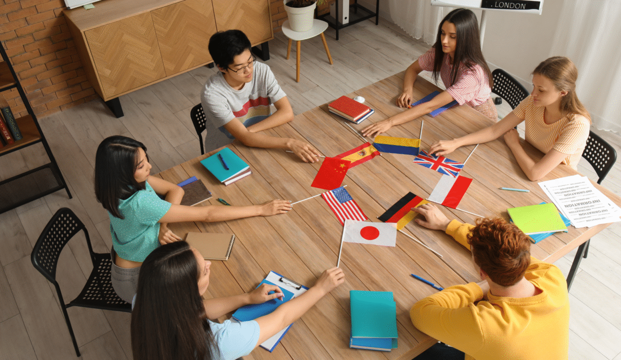 Students from diverse backgrounds sit around a table holding various national flags during a classroom activity, reflecting the multicultural environment offered by Bali international schools.