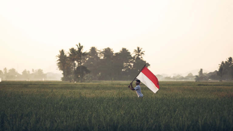 A student running through vast rice fields while holding an Indonesian flag symbolizing permanent residency in Indonesia