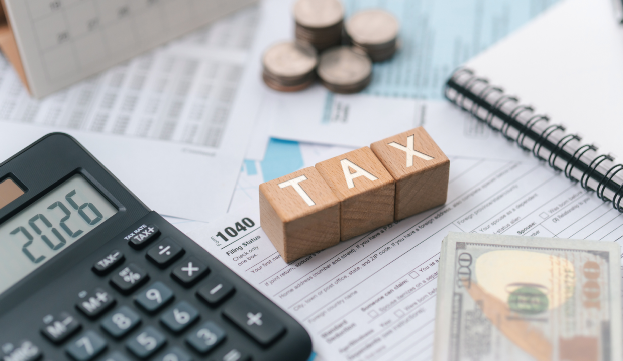 Property sales tax concept illustrated with tax documents, calculator, cash, and wooden blocks spelling tax on a financial desk.