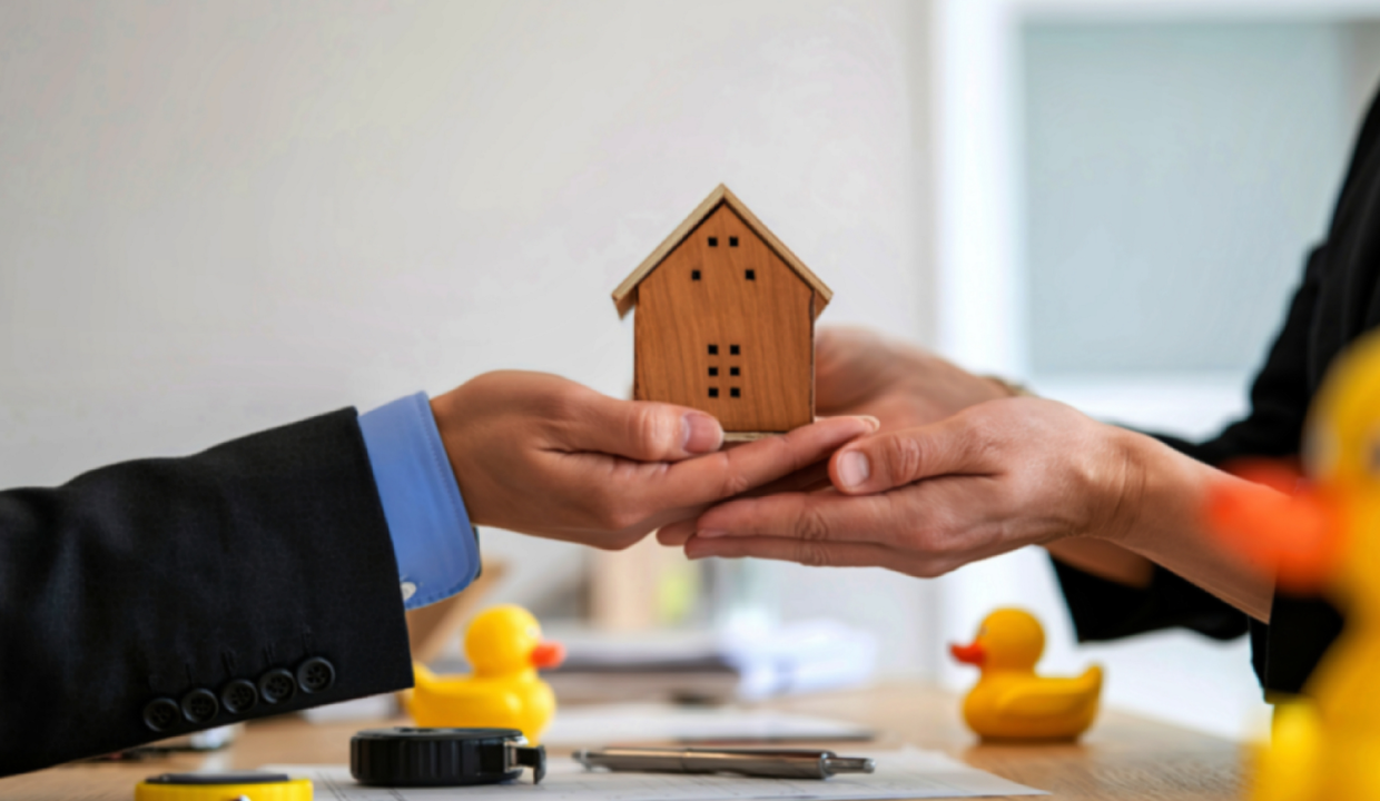Hands exchanging a wooden house model over a desk, symbolizing foreign property ownership in Bali and legal property transfer agreements.