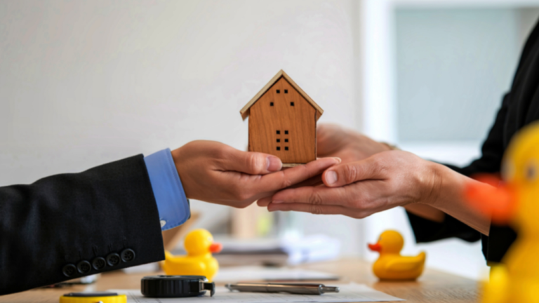 Hands exchanging a wooden house model over a desk, symbolizing foreign property ownership in Bali and legal property transfer agreements.