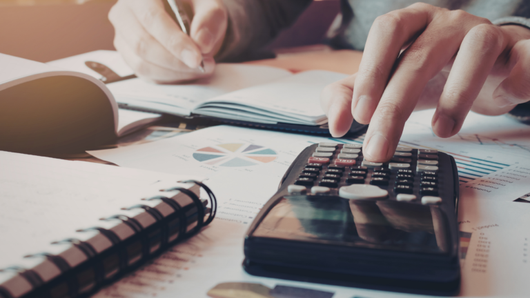 Hands using a calculator and financial reports to perform villa rental business calculations in Bali for foreign property investors.